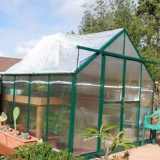 A Grandio shade net is covering an Ascent greenhouse to help regulate the temperature inside. There's a roof-window that's opened under the shade net, showing that the shade net is elastic enough to continue covering the roof while allowing the roof window to ventilate air.